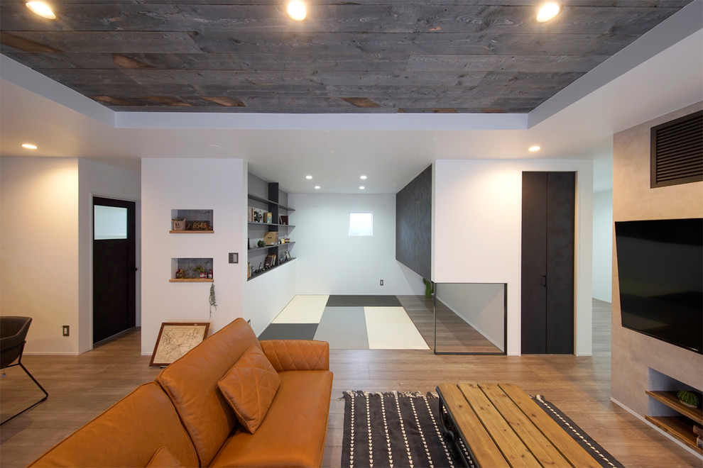 Cette image montre une salle de séjour urbaine ouverte avec un mur blanc, un sol en bois brun, un téléviseur fixé au mur et un sol marron.