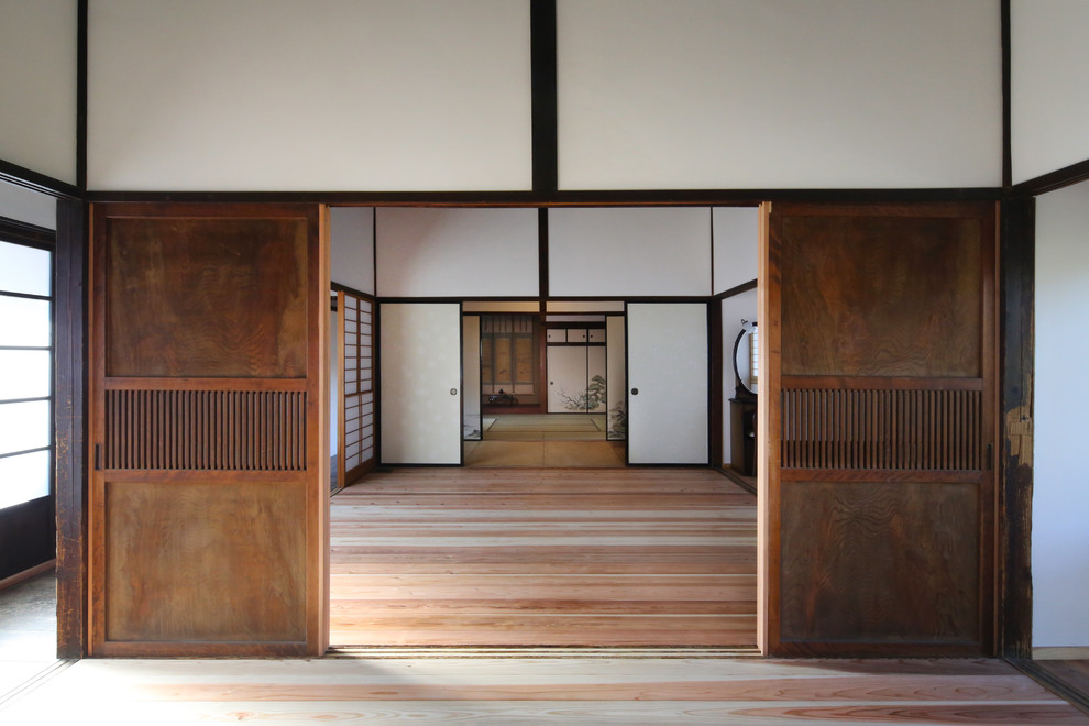 Exemple d'une salle de séjour asiatique avec un mur blanc et un sol en bois brun.