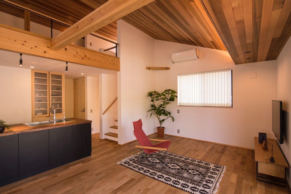 Aménagement d'une salle de séjour asiatique ouverte avec un mur blanc, un sol en bois brun, un téléviseur fixé au mur et un sol marron.
