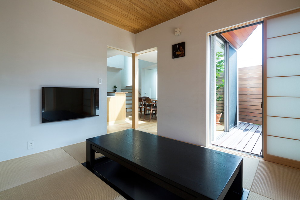 Aménagement d'une salle de séjour asiatique avec un mur blanc, un sol de tatami, un téléviseur fixé au mur et un sol vert.