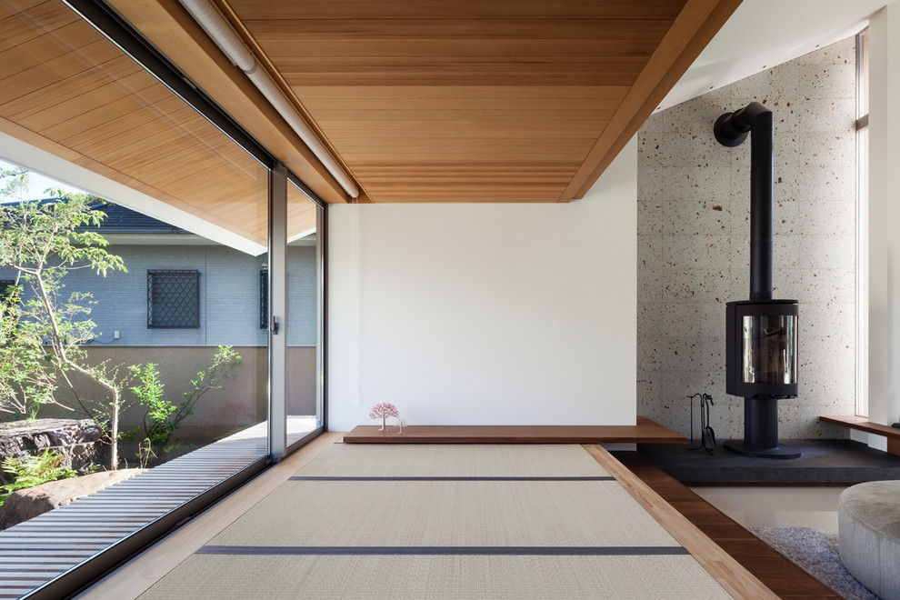 Aménagement d'une salle de séjour contemporaine avec un mur blanc, un sol de tatami, un poêle à bois, un manteau de cheminée en pierre et un sol vert.