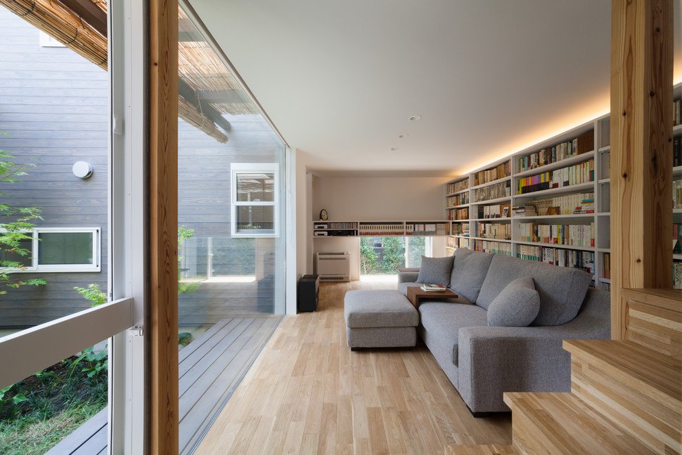Cette image montre une salle de séjour design fermée avec une bibliothèque ou un coin lecture, un mur blanc, aucun téléviseur, parquet clair et un sol beige.