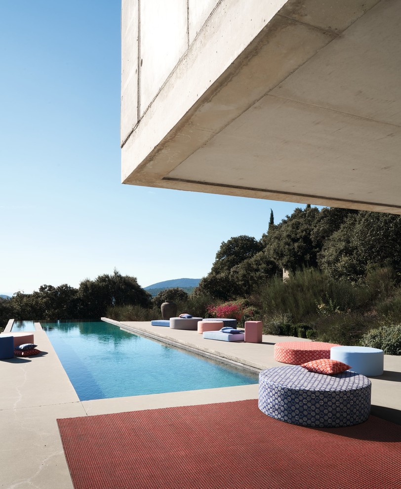 Ispirazione per una piscina a sfioro infinito design rettangolare dietro casa con lastre di cemento