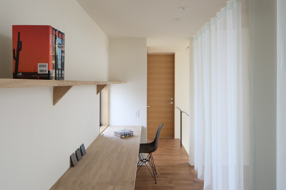 Diseño de despacho minimalista con paredes blancas, suelo de madera en tonos medios, escritorio empotrado y suelo marrón