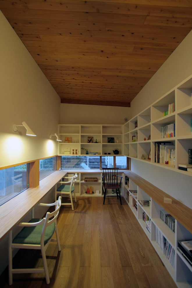 Asiatisk inredning av ett hemmabibliotek, med vita väggar, mellanmörkt trägolv, ett inbyggt skrivbord och brunt golv