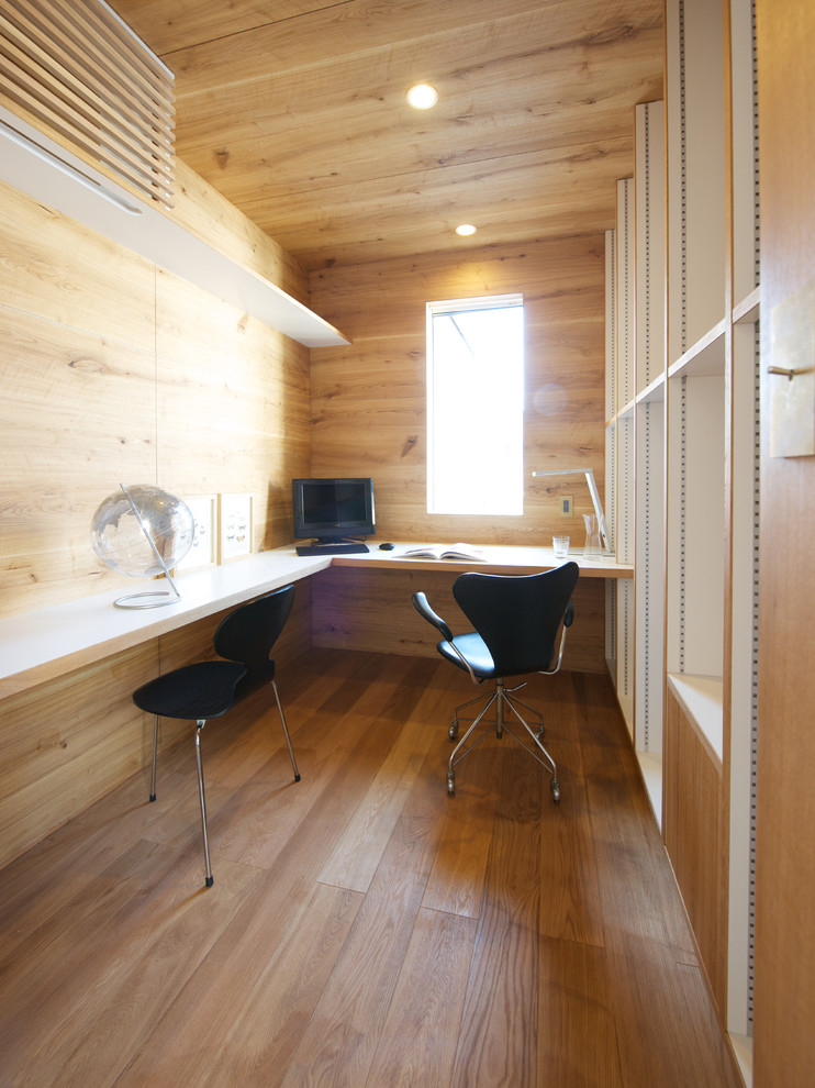 Cette photo montre un bureau scandinave avec une bibliothèque ou un coin lecture, un mur marron, un sol en bois brun et un bureau intégré.