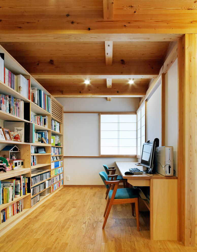 Inredning av ett asiatiskt hemmabibliotek, med vita väggar, ljust trägolv och ett inbyggt skrivbord