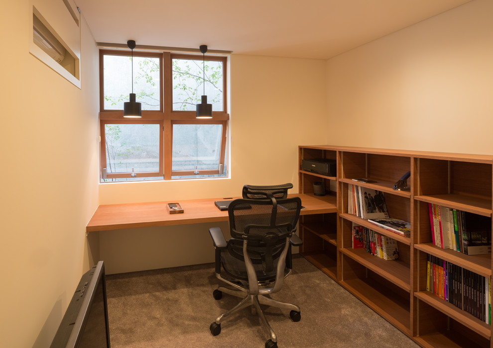 This is an example of a modern study in Kobe with white walls, carpet, no fireplace, a built-in desk and beige floors.