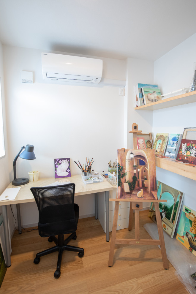 Bild på ett litet hemmastudio, med vita väggar, målat trägolv, ett fristående skrivbord och beiget golv