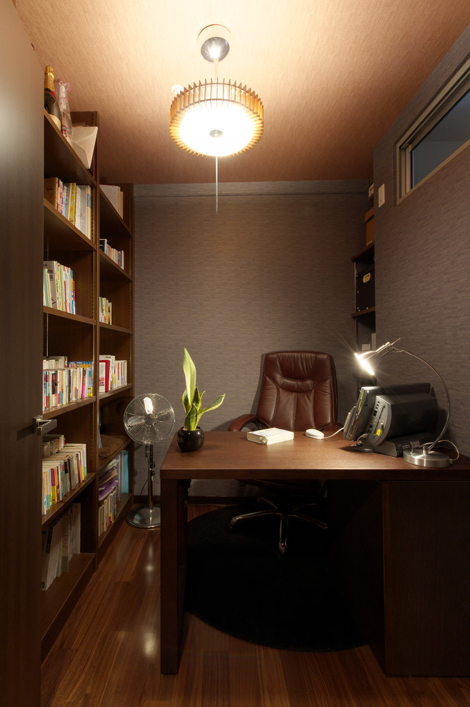 Cette image montre un petit bureau minimaliste avec un mur gris, un sol en bois brun, un bureau indépendant et un sol marron.