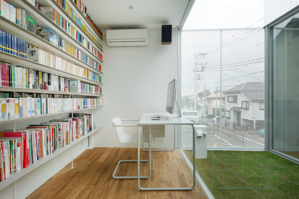 Aménagement d'un bureau moderne avec une bibliothèque ou un coin lecture, un mur blanc, un sol en bois brun, un bureau indépendant et un sol marron.