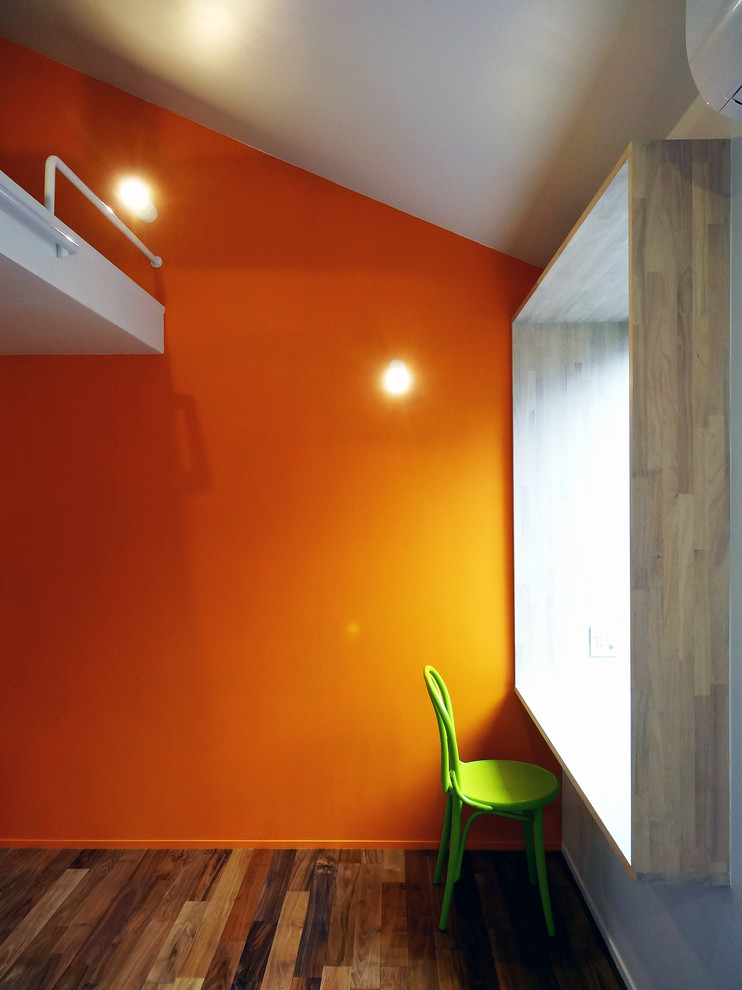 Aménagement d'un bureau moderne de taille moyenne avec un mur orange, un sol en bois brun, un bureau intégré et un sol marron.
