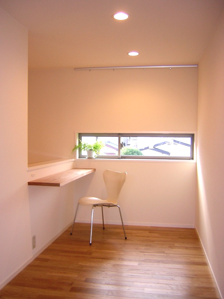 Aménagement d'un petit bureau asiatique avec un mur blanc, un sol en bois brun, aucune cheminée, un bureau intégré et un sol marron.