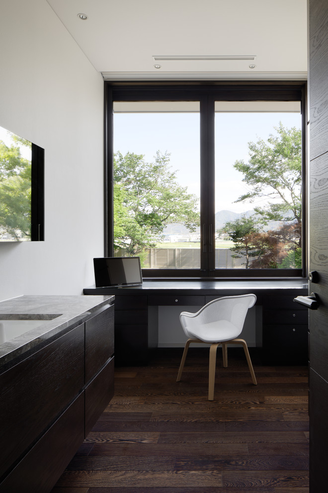 Стильный дизайн: кабинет в современном стиле с белыми стенами, темным паркетным полом, встроенным рабочим столом и коричневым полом - последний тренд