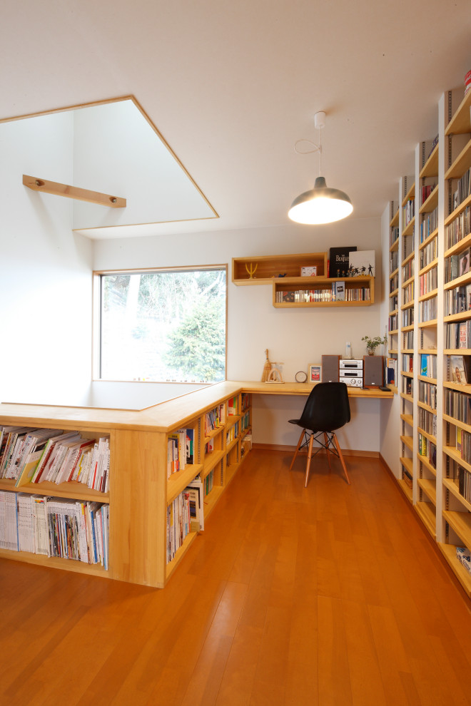 Modernes Arbeitszimmer mit weißer Wandfarbe, braunem Holzboden, Einbau-Schreibtisch und braunem Boden in Sonstige