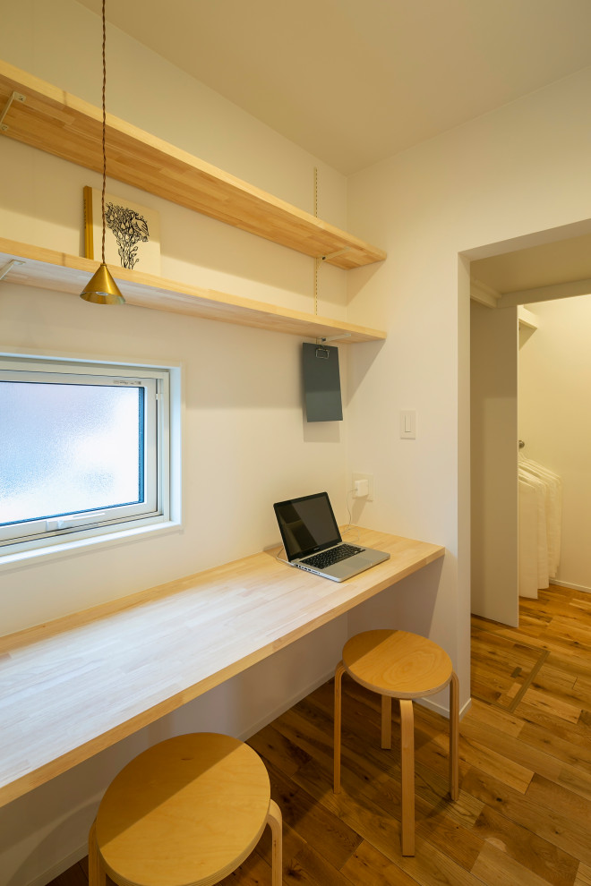 Kleines Skandinavisches Arbeitszimmer ohne Kamin mit Arbeitsplatz, weißer Wandfarbe, braunem Holzboden, Einbau-Schreibtisch und beigem Boden in Sonstige
