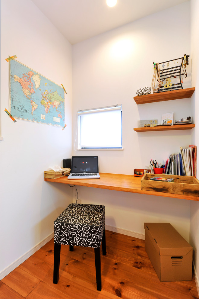 他の地域にある小さな北欧スタイルのおしゃれなホームオフィス・書斎 (白い壁、無垢フローリング、造り付け机、茶色い床) の写真