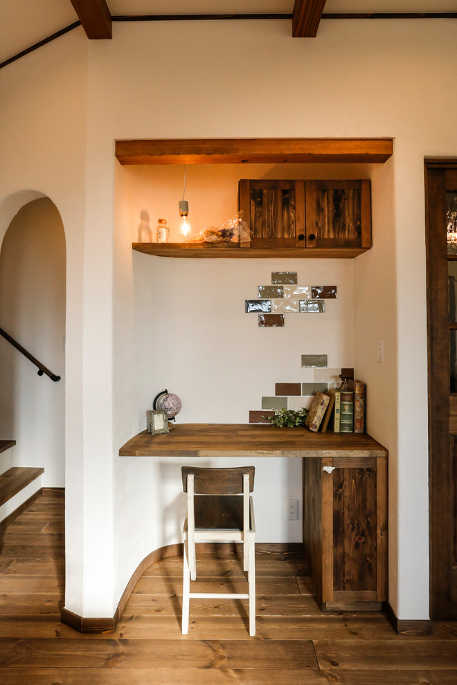 Immagine di uno studio mediterraneo con pareti bianche, pavimento in legno massello medio, scrivania incassata e pavimento marrone
