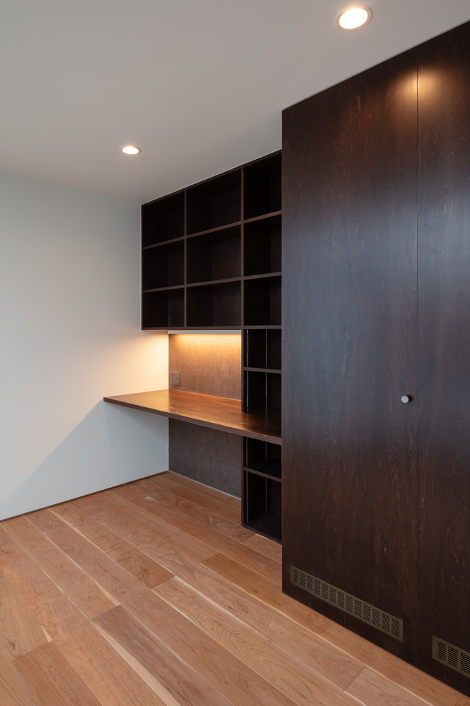 Modernes Arbeitszimmer mit Arbeitsplatz, brauner Wandfarbe, Sperrholzboden, Einbau-Schreibtisch und braunem Boden in Sonstige
