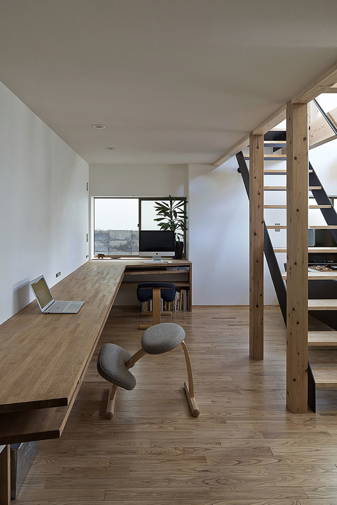Idee per uno studio nordico con pareti bianche, pavimento in legno verniciato, scrivania incassata e pavimento marrone