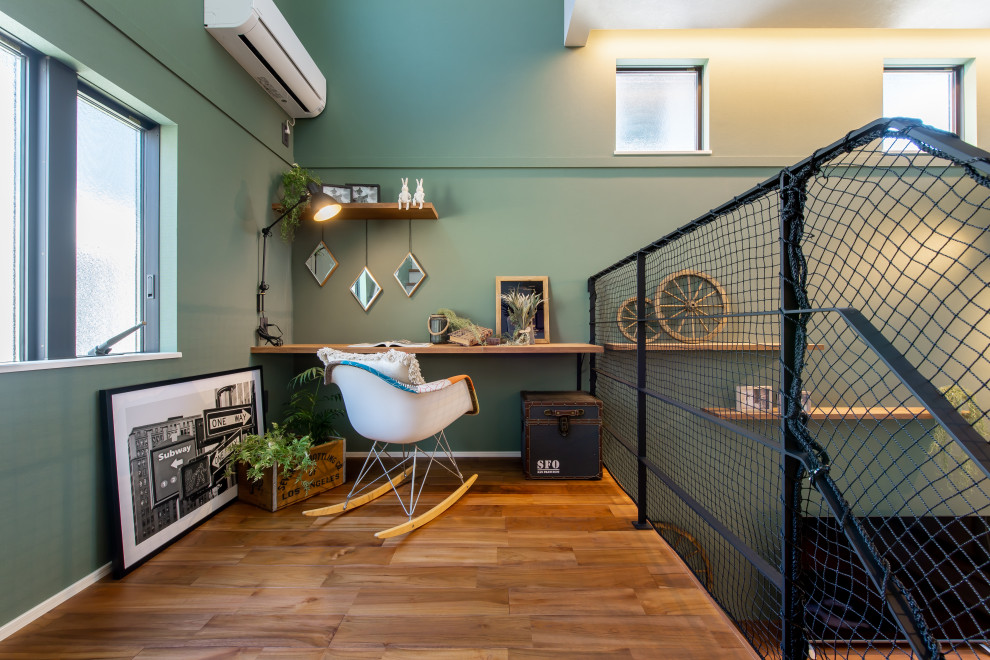 Modelo de despacho de tamaño medio con paredes verdes, suelo de madera en tonos medios, escritorio empotrado, papel pintado y papel pintado