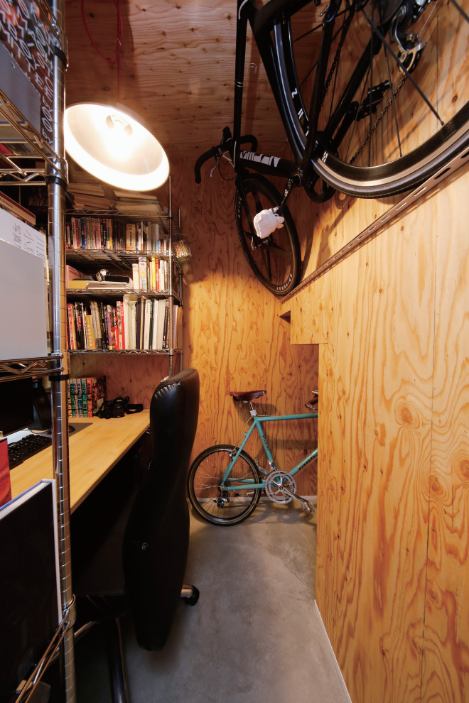 Bild på ett mellanstort industriellt hemmabibliotek, med bruna väggar, betonggolv, ett inbyggt skrivbord och grått golv