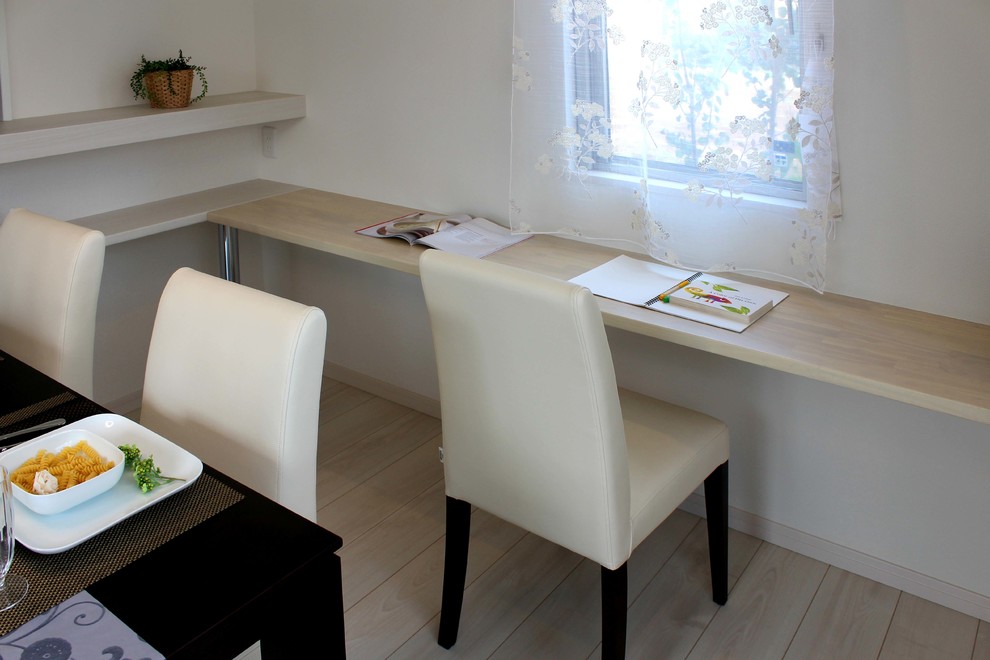 Ejemplo de despacho actual con biblioteca, paredes blancas, suelo de madera clara, escritorio empotrado y suelo beige