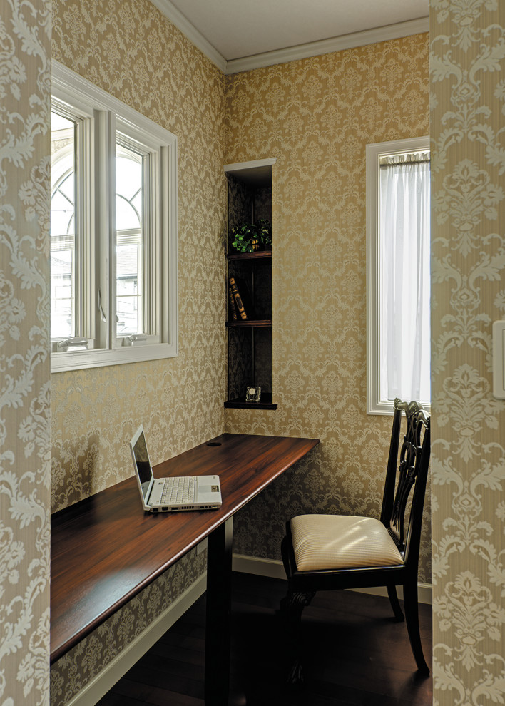 Modelo de despacho tradicional con paredes beige, suelo de contrachapado, escritorio empotrado, suelo marrón, papel pintado y papel pintado