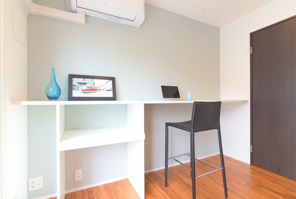 Cette photo montre un bureau moderne avec un mur blanc, un sol en bois brun, aucune cheminée et un bureau intégré.
