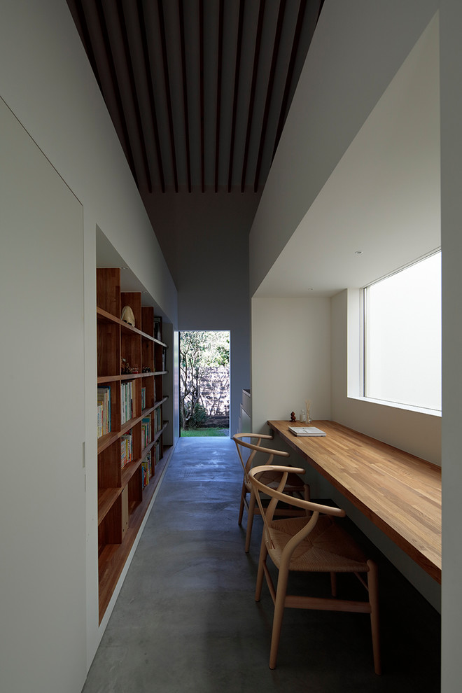 Cette image montre un bureau design avec un mur blanc, sol en béton ciré, un bureau intégré et un sol gris.