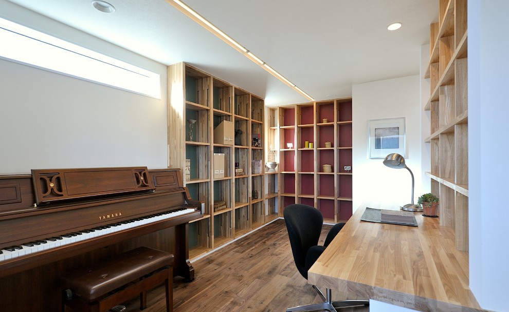Exempel på ett asiatiskt hemmabibliotek, med vita väggar, mellanmörkt trägolv, ett inbyggt skrivbord och brunt golv
