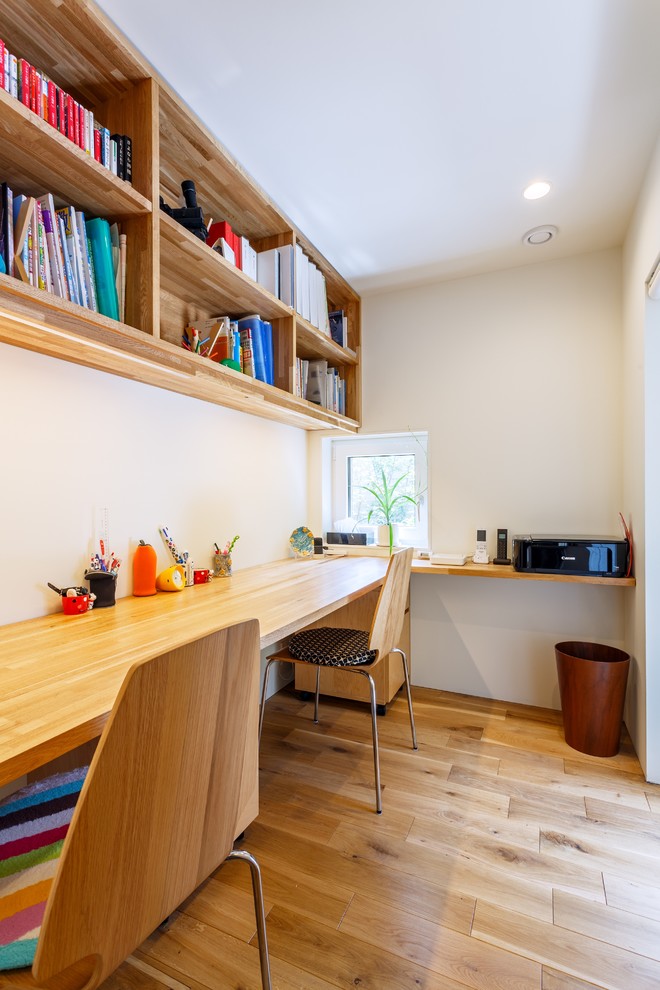 Immagine di uno studio moderno con pareti bianche, pavimento in legno massello medio, scrivania incassata e pavimento marrone