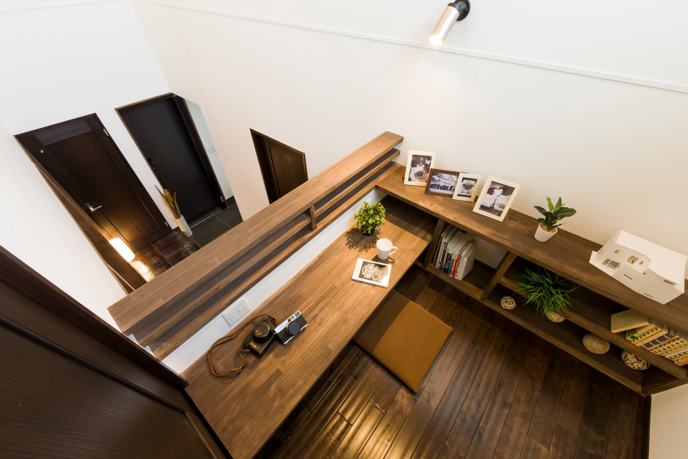 Пример оригинального дизайна: кабинет с белыми стенами, темным паркетным полом, встроенным рабочим столом и коричневым полом