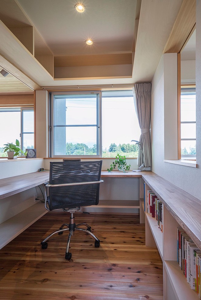 This is an example of a world-inspired home office in Other with white walls, medium hardwood flooring, a built-in desk and brown floors.