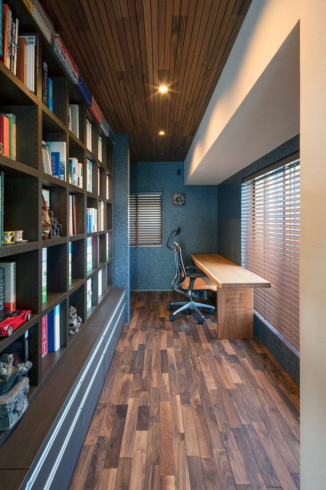 Cette photo montre un bureau moderne avec un mur bleu, parquet foncé, un bureau intégré et un sol marron.