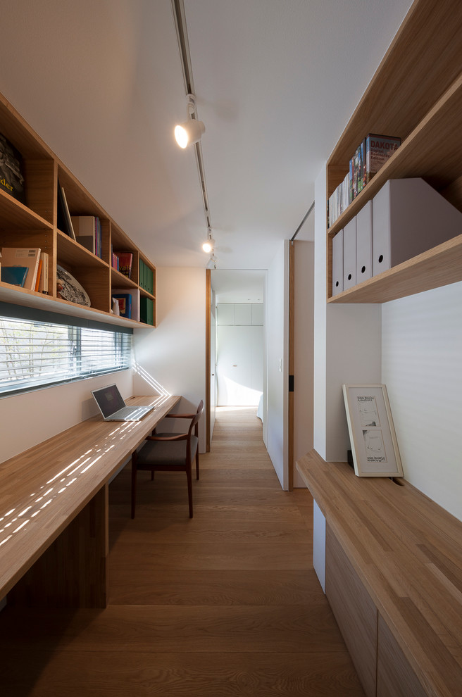 Modern inredning av ett litet hemmabibliotek, med ett inbyggt skrivbord och vita väggar
