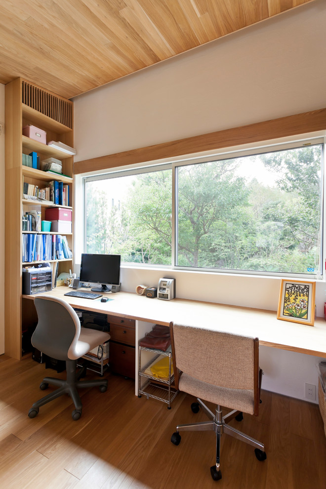 Cette photo montre un bureau asiatique de taille moyenne avec un mur blanc, un sol en bois brun, un bureau intégré et un sol marron.
