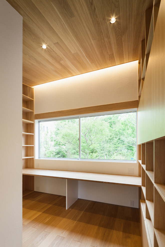 Foto de despacho minimalista de tamaño medio con paredes blancas, suelo de madera en tonos medios, escritorio empotrado y suelo marrón