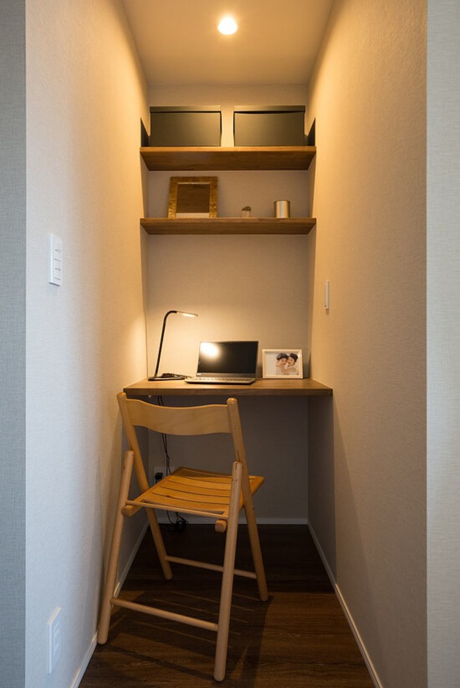 Cette image montre un petit bureau minimaliste avec un mur gris, parquet foncé, un bureau intégré et un sol marron.