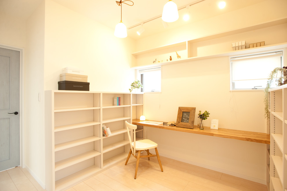 Diseño de despacho escandinavo pequeño con paredes blancas, suelo de madera clara, escritorio empotrado y suelo marrón