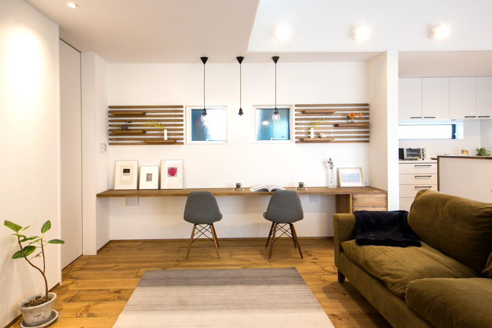 Ejemplo de despacho actual con paredes blancas, suelo de madera en tonos medios, escritorio empotrado y suelo marrón