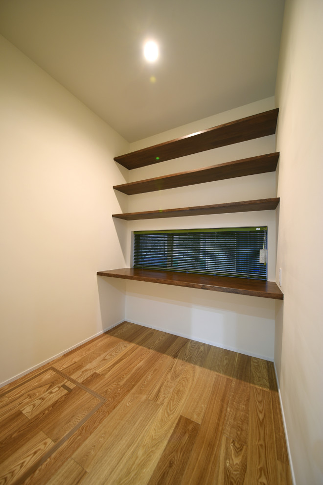 Cette image montre un grand bureau minimaliste avec un mur blanc, un sol en bois brun, aucune cheminée, un bureau intégré et un sol marron.