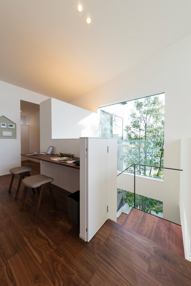 Modernes Arbeitszimmer ohne Kamin mit weißer Wandfarbe, dunklem Holzboden, Einbau-Schreibtisch und braunem Boden in Sonstige