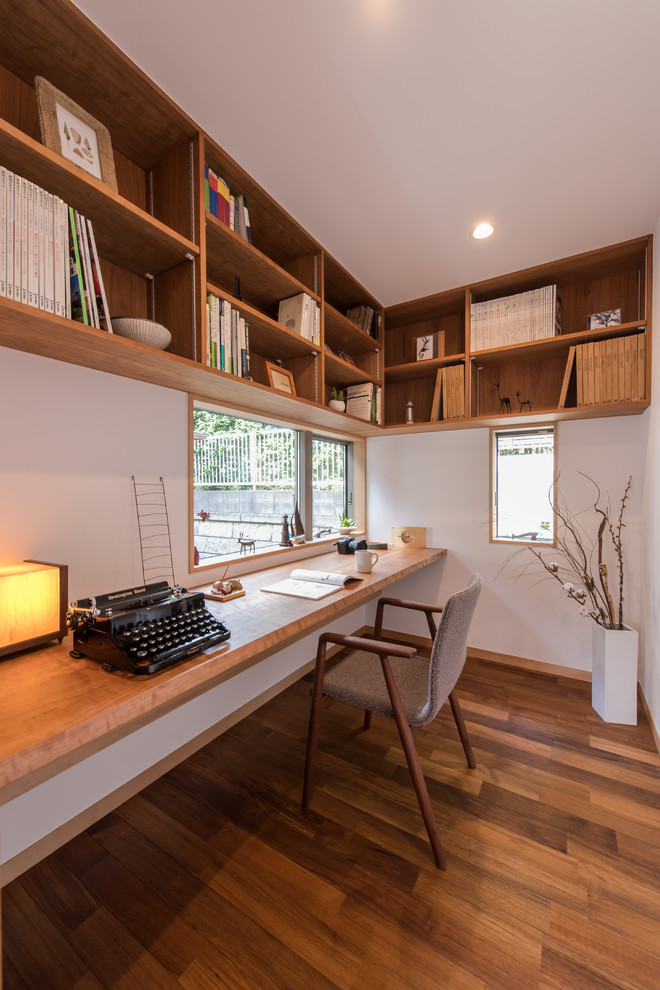 Стильный дизайн: кабинет в восточном стиле с белыми стенами, паркетным полом среднего тона, встроенным рабочим столом и коричневым полом - последний тренд