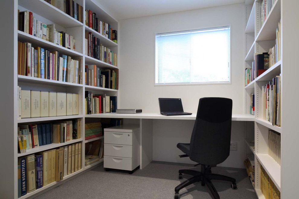 Bild på ett litet funkis hemmabibliotek, med vita väggar, heltäckningsmatta, ett inbyggt skrivbord och grått golv