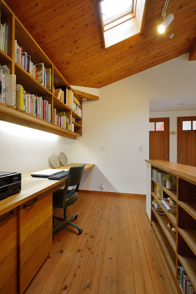 This is an example of a world-inspired home office in Other with white walls, medium hardwood flooring, a built-in desk and brown floors.
