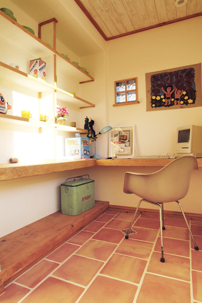 Diseño de despacho de estilo americano con paredes blancas, suelo de baldosas de terracota, escritorio empotrado y suelo marrón