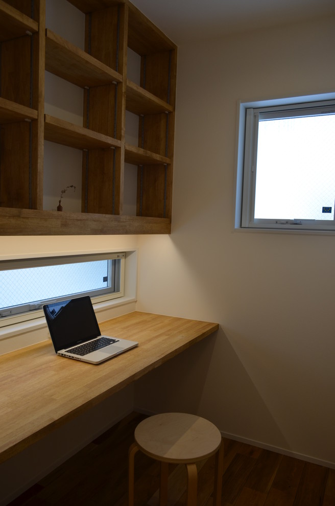 Modelo de despacho urbano de tamaño medio sin chimenea con paredes blancas, suelo de madera en tonos medios, escritorio empotrado y suelo beige