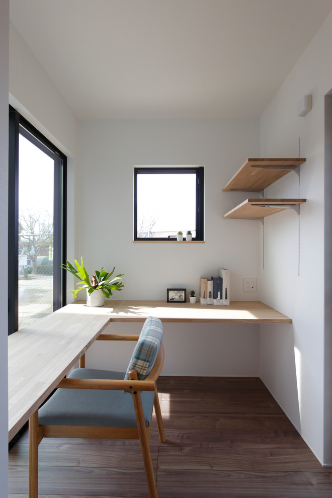 Modelo de despacho moderno pequeño con paredes blancas, suelo de madera oscura, escritorio empotrado y suelo marrón