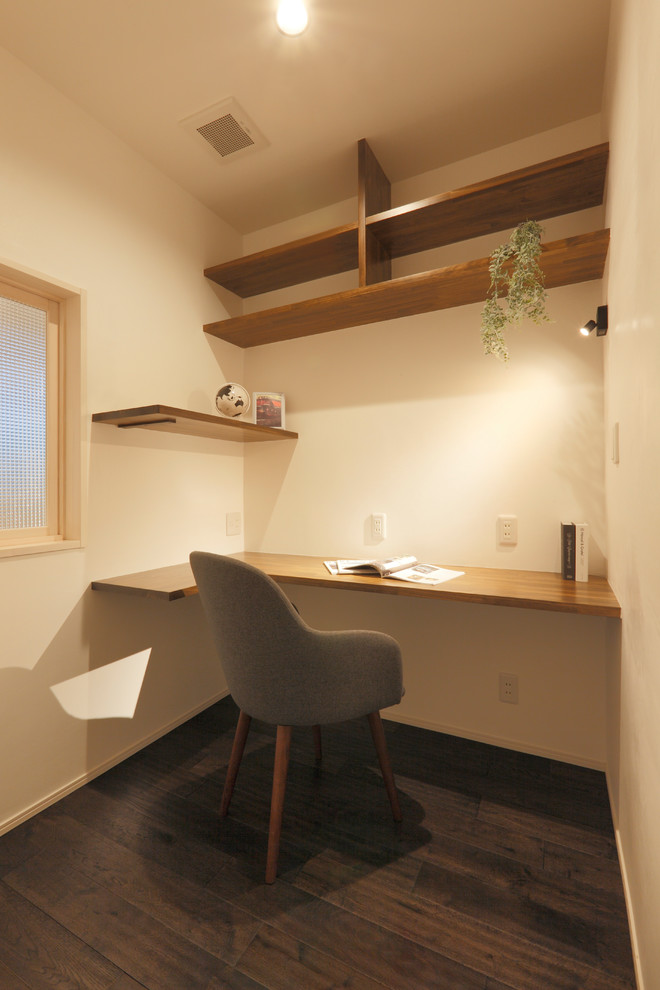 На фото: рабочее место в стиле модернизм с белыми стенами, темным паркетным полом, встроенным рабочим столом и коричневым полом с